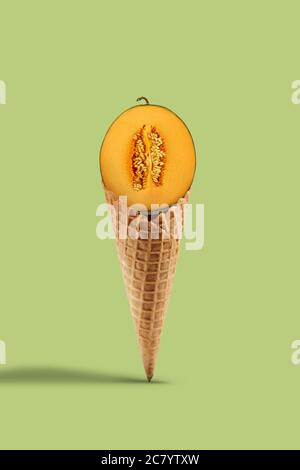 Half a ripe yellow melon in sweet wafer cone over light green background. Healthy nutrition, seasonal harvest of fruits. Close up, copy space Stock Photo