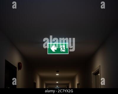 Fire exit. Illuminated green emergency exit sign hanging on ceiling in modern building in the dark in apartment. Stock Photo
