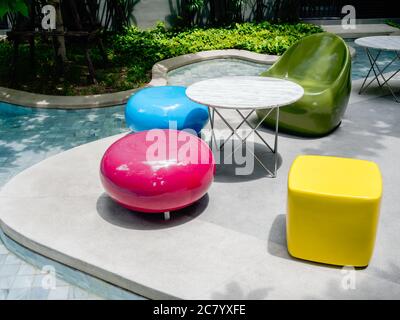 Modern bright colors chairs and a variety of shapes and round tables beside the outdoor swimming pool. Empty colorful furniture decoration near the po Stock Photo