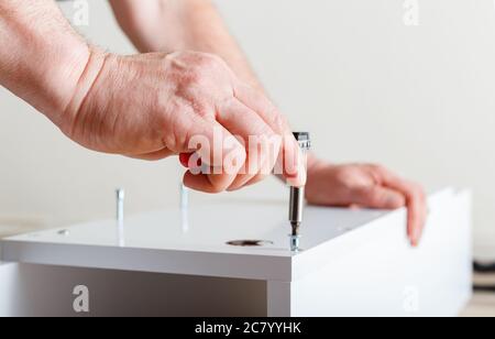 Furniture assembly. Male hands master collects furniture using screwdriver tools, instrument at home. Moving, home improvement, furniture repair and Stock Photo