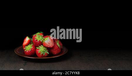 Strawberry fruit in a bowl against dark background. Stock Photo