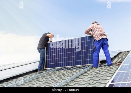 Electrical engineers mans are working installing solar panels on solar station on house roof against blue sky in sunny day. Development sun Stock Photo