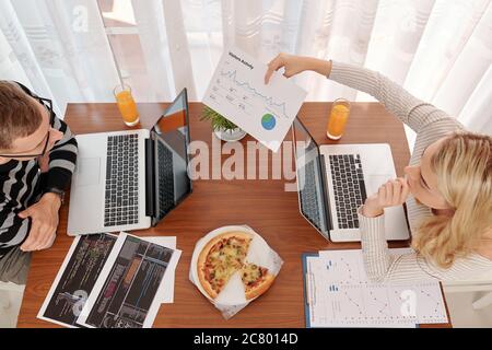 Young woman showing visitors activity chart to her husband programmer when they are working on new mobile application at home Stock Photo