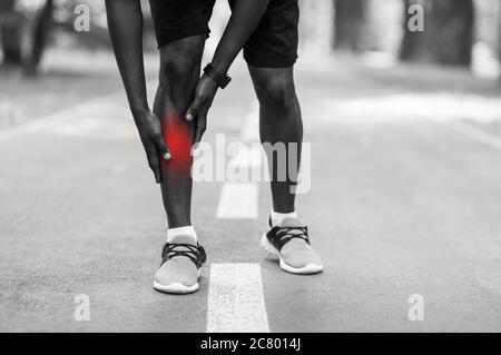 Closeup of african sportsman touching injured leg Stock Photo
