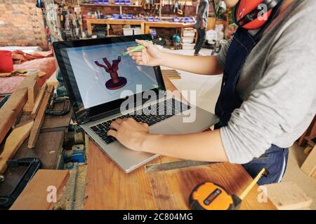 Female carpenter making 3D model of dinner table on laptop before making it Stock Photo