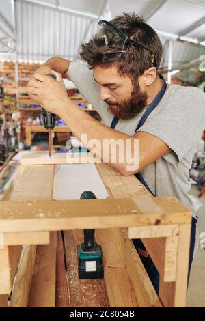 Concentrated young carpenter driving screws into wooden stool Stock Photo