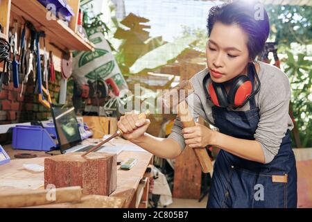 Concentrated Vietnamese carpenter using chisel and hammer when carving wood Stock Photo