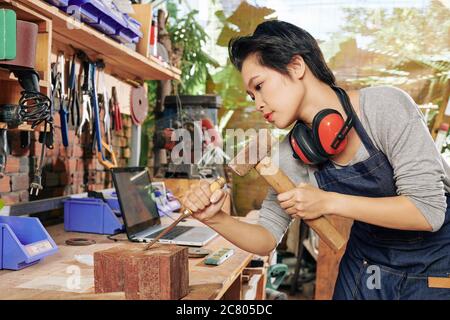 Vietnamese female carpenter using chisel and hammer when working with hard wood Stock Photo