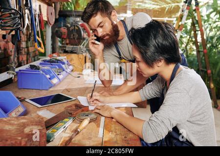 Carpenter talking on phone with customer when his female colleague writing details of order on sheet of paper Stock Photo
