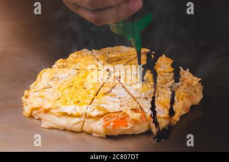 Japanese pizza okonomiyaki cooking on hot plate teppanyaki style. Stock Photo