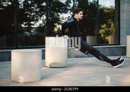 Side view of young attractive sporty man doing exercises during workout in park Stock Photo