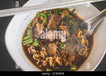 Braised pork noodles in Thai style with indoor low lighting. Stock Photo