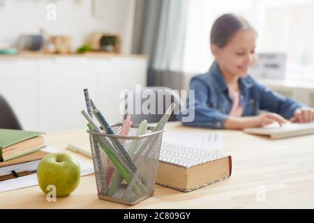 Background image of girl using laptop while studying at home, focus on pencil stand and books, copy space Stock Photo