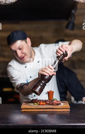 Chef sprinkling spices on dish in commercial kitchen Stock Photo