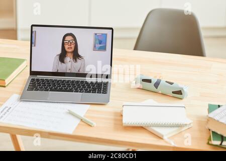 Background image of wooden desk with school supplies and laptop with female teacher giving video lesson or online class on screen standing on wooden d