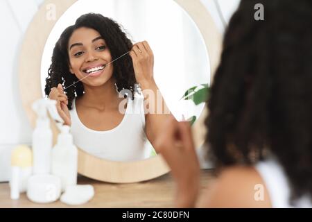 Happy black woman flossing teeth with dental floss in front of mirror Stock Photo