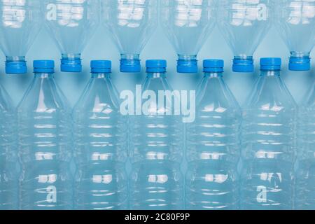 Horizontal color image with a front view of an empty clear plastic bottles with caps stacked on a blue background. Recycling and environment concept. Stock Photo