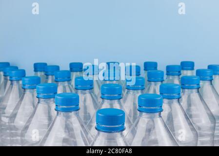 Horizontal color image with a front view of an empty clear plastic bottles with caps stacked on a blue background. Recycling and environment concept. Stock Photo