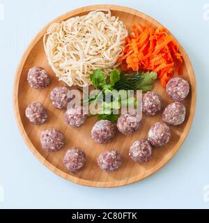 Raw meatballs and frozen noodles on a wooden plate. Top view. Stock Photo