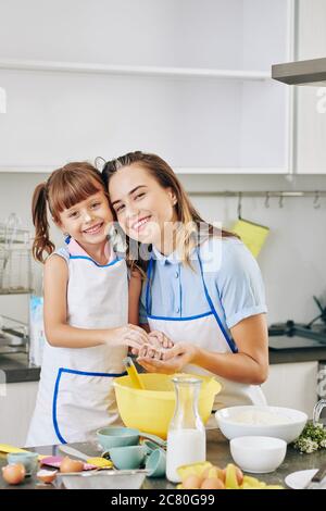 Portrait of happy smiling pretty woman and her little daughter hugging and looking at camera after making dough Stock Photo