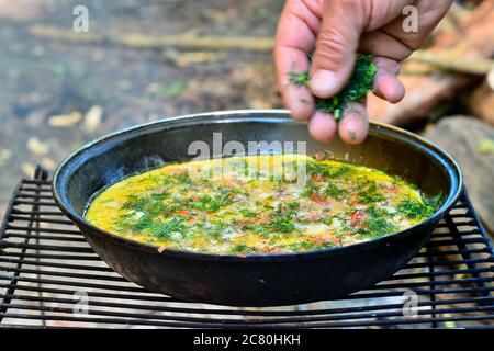 A man's hand in a blurry motion sprinkles dill greens on an open-air fried egg in a frying pan Stock Photo