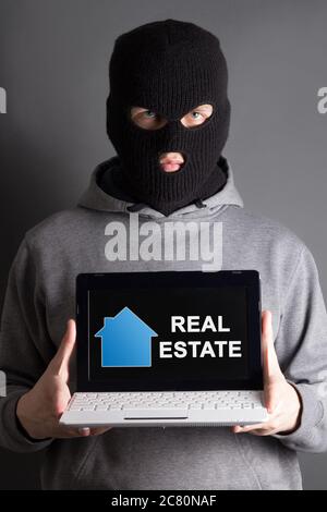 burglary and home safety concept -masked man holding computer with real estate site Stock Photo