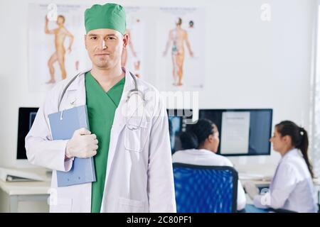 Portrait of smiling confident general practitioner in rubber gloves holding folder with medical documents and looking at camera Stock Photo