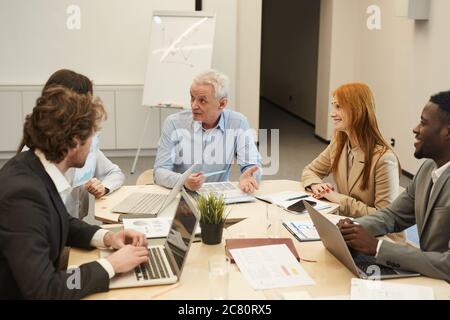 Portrait of white haired mature businessman gesturing while talking to employees during meeting in conference room, copy space Stock Photo