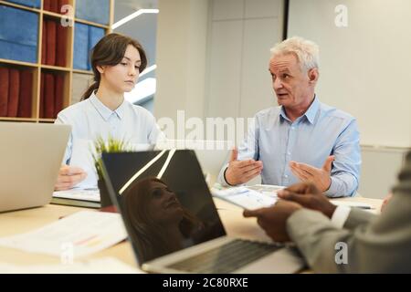 Portrait of white haired mature businessman gesturing actively while talking to employees during meeting in conference room, copy space Stock Photo