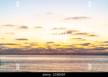 The dawn sky over the Thanet Offshore wind farm off the kent Coast at Broadstairs. Clouds on the horizon with orange and yellow sky over a calm sea. Stock Photo