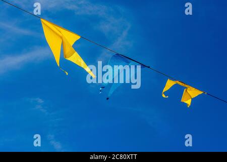 Colorful flags sway gently in the breeze against a bright blue sky above a festive outdoor event Stock Photo