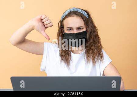 Little kid schoolgirl 12-13 years old in face mask study at desk with pc laptop isolated on orange background. School distance education at home Stock Photo