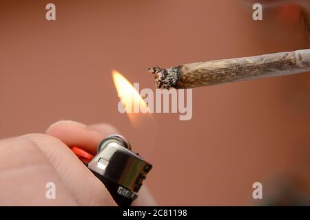 Lighting a rolled herbal cigarette with a lighter in an outdoor setting during daylight Stock Photo
