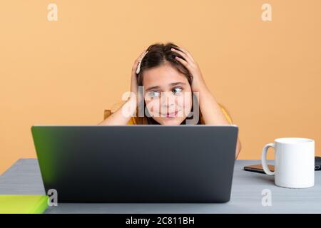 Exhausted schoolchild sitting at desk near laptop and copy book while doing schoolwork at home Stock Photo