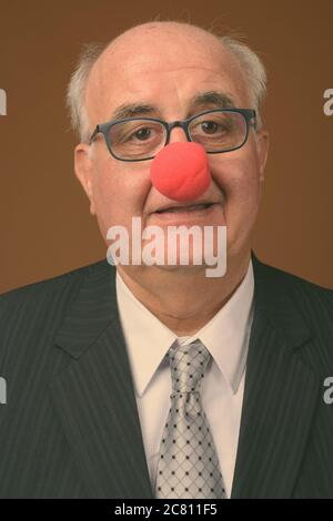 Overweight senior businessman wearing clown's nose against brown background Stock Photo