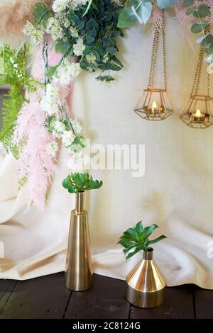 Wedding decoration, floristry. Succulents in gold vessels near the table with a light tablecloth. Stock Photo