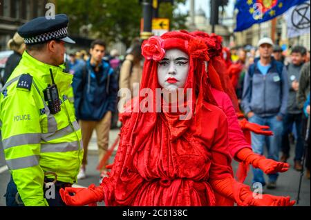 LONDON - OCTOBER 18, 2019: Close up of the Extinction Rebellion Red Brigade protesters passing a Metropolitan Police Officer