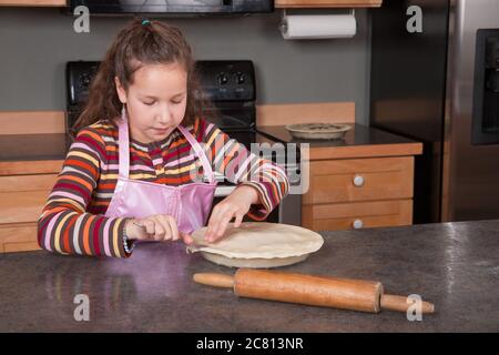 Eleven year old girl placing pie dough on top of pie and crimping the edges Stock Photo