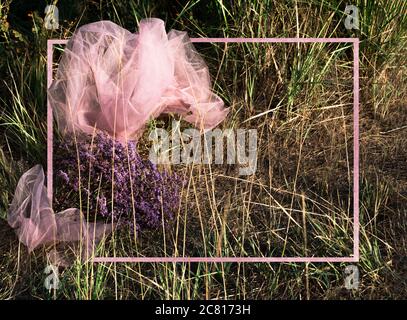 Grass field with scarf and bouquet of wild flowers background with pink border. The view from the top. Stock Photo
