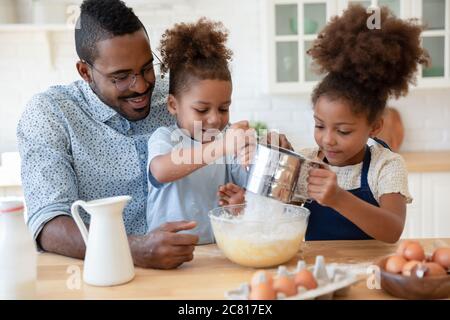 Caring biracial dad and little kids making pancakes Stock Photo