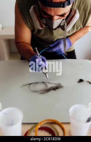 Close up of airbrush painter with mask drawing an eye on a paper. Stock Photo