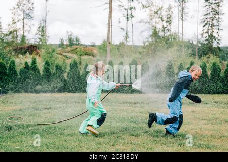 sister spraying her brother with a hose whilst playing in the rain Stock Photo