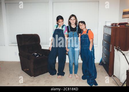 Three siblings smile while all wearing overalls and two oversized Stock Photo