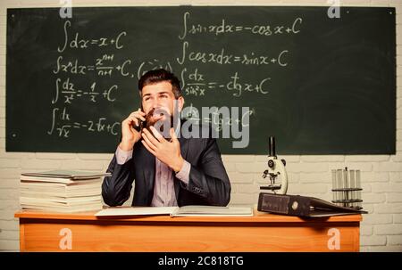 Calling parents. School teacher call mobile phone while sit classroom chalkboard background. Teacher bearded man talk mobile phone. Call colleague ask advice. Pedagogue keep in touch with colleagues. Stock Photo