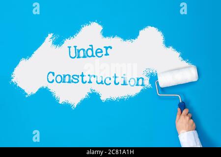 Hand with paint roller paints blue wall and "under construction" sign on it. Stock Photo
