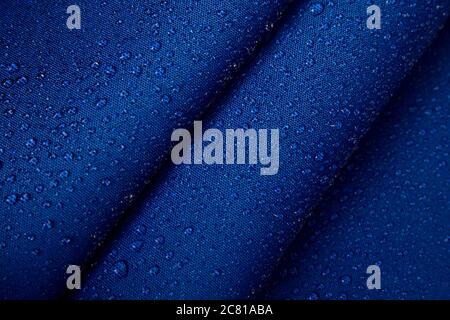 Abstract background of hydrophobic fabric. Drops of water on creased blue fabric. Stock Photo