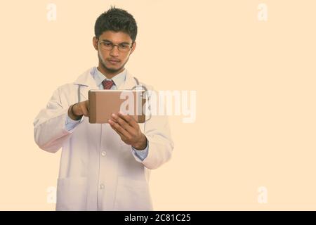 Studio shot of young handsome Indian man doctor using digital tablet Stock Photo