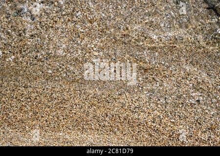 Small pebbles and sand seabed background texture under clear crystal shallow sea water, top view. Stock Photo