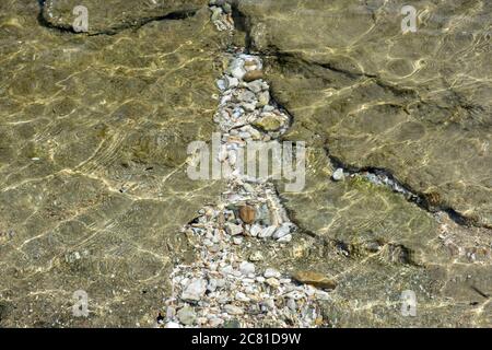 Seabed background texture under clear crystal shallow sea water, top view. Small pebbles, sand and green rock Stock Photo