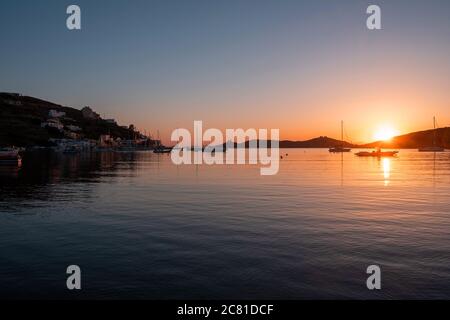 Kea island, Greece. Sunset orange color over sea water. Boats anchored at Vourkari port, golden reflections on the rippled water, Aegean Mediterranean Stock Photo